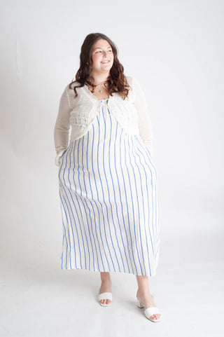 Woman wearing a long white dress with blue stripes against a white background