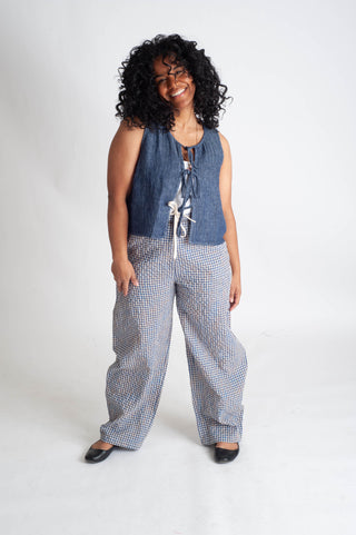 Woman wearing a denim sleeveless top and checkered pants on a white background