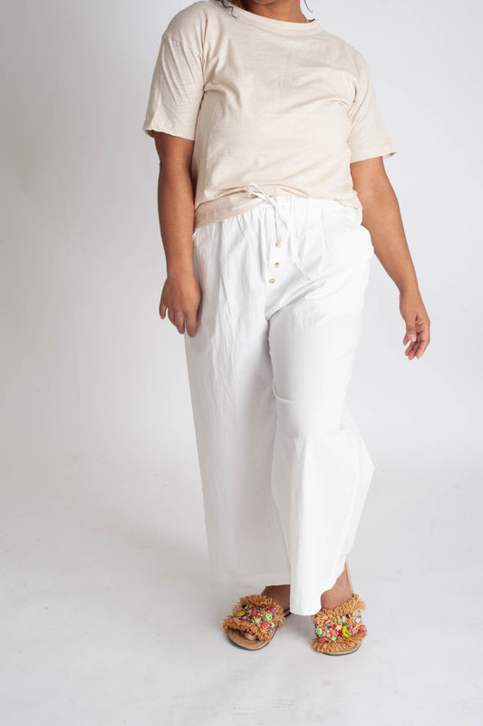 Person wearing a beige t-shirt and white pants on a white background