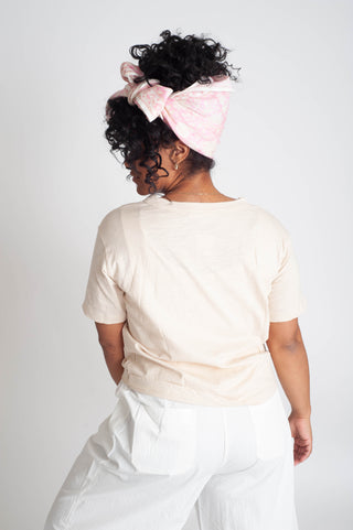 Woman wearing a light pink top and white pants with a pink headscarf on a white background