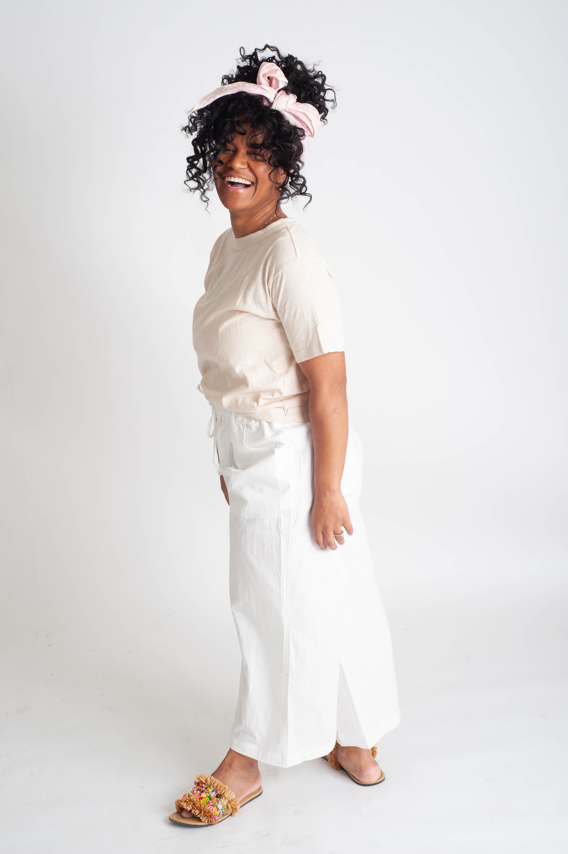 Woman wearing a beige top and white pants with a pink headband on a white background