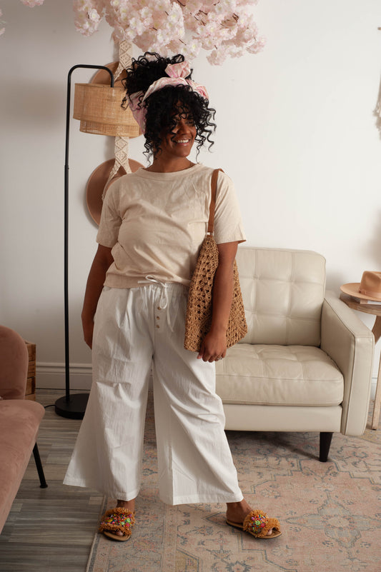 Woman standing in a living room wearing a beige top and white pants