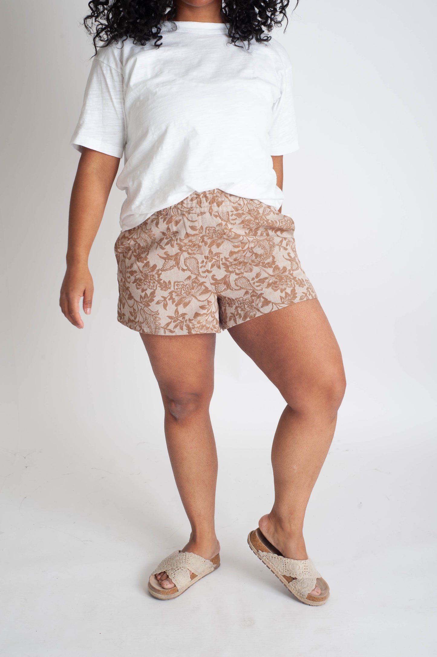 Person wearing a white t-shirt and beige patterned shorts on a plain background