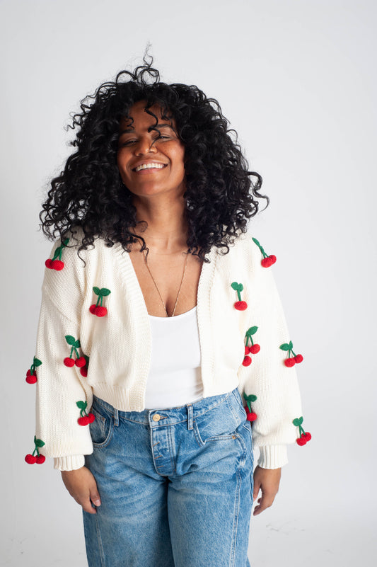 Person wearing a white cardigan with cherry decorations on a plain background