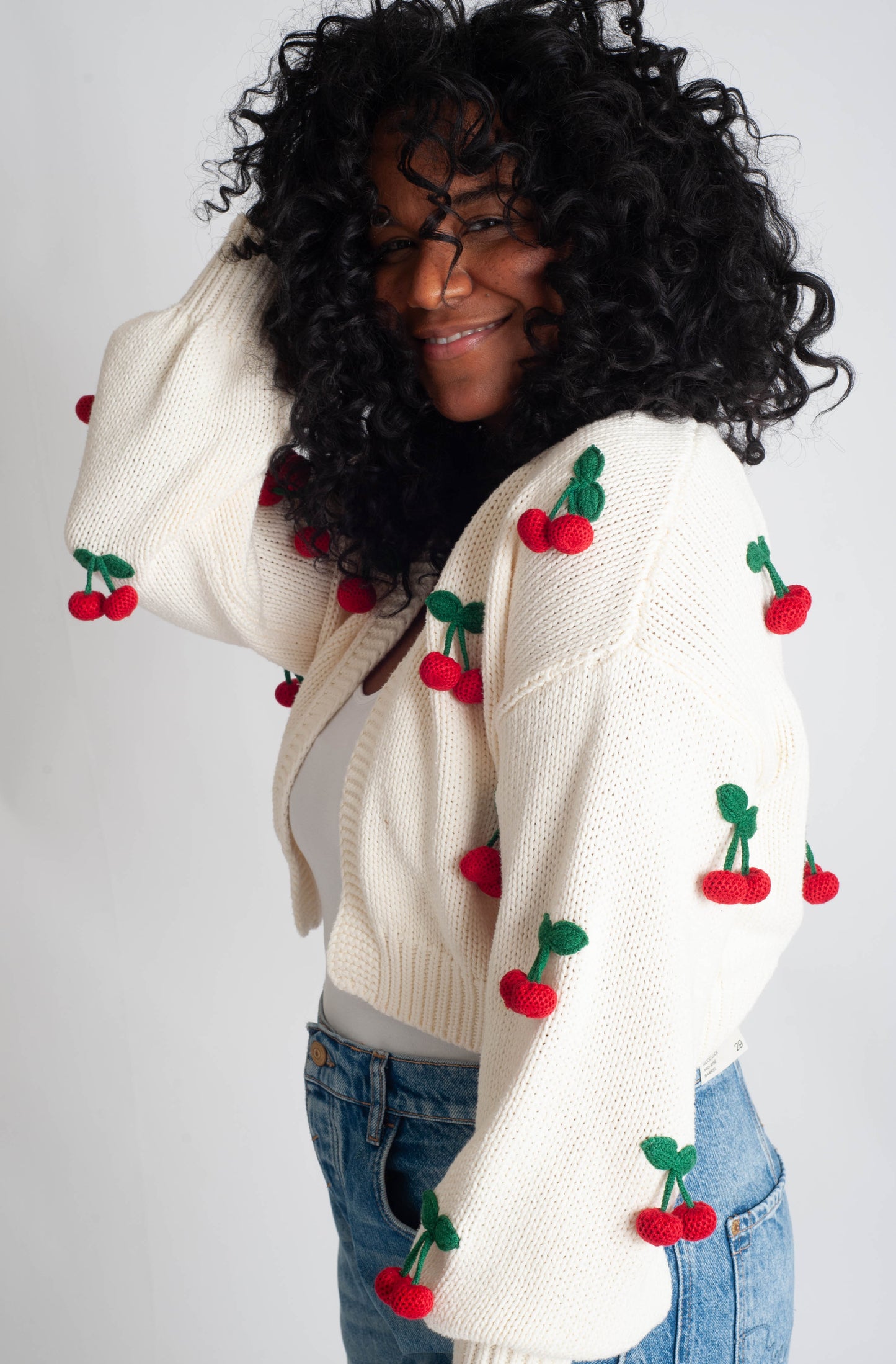 Person wearing a white cardigan with cherry decorations on a plain background