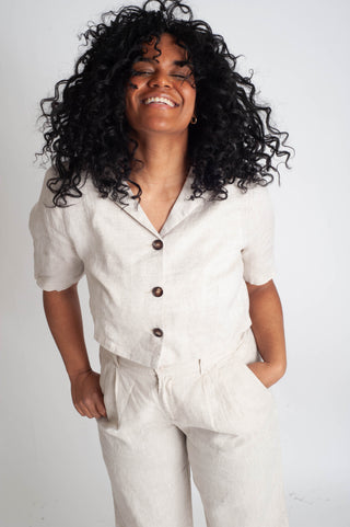 Person wearing a light-colored outfit with buttons on a plain background