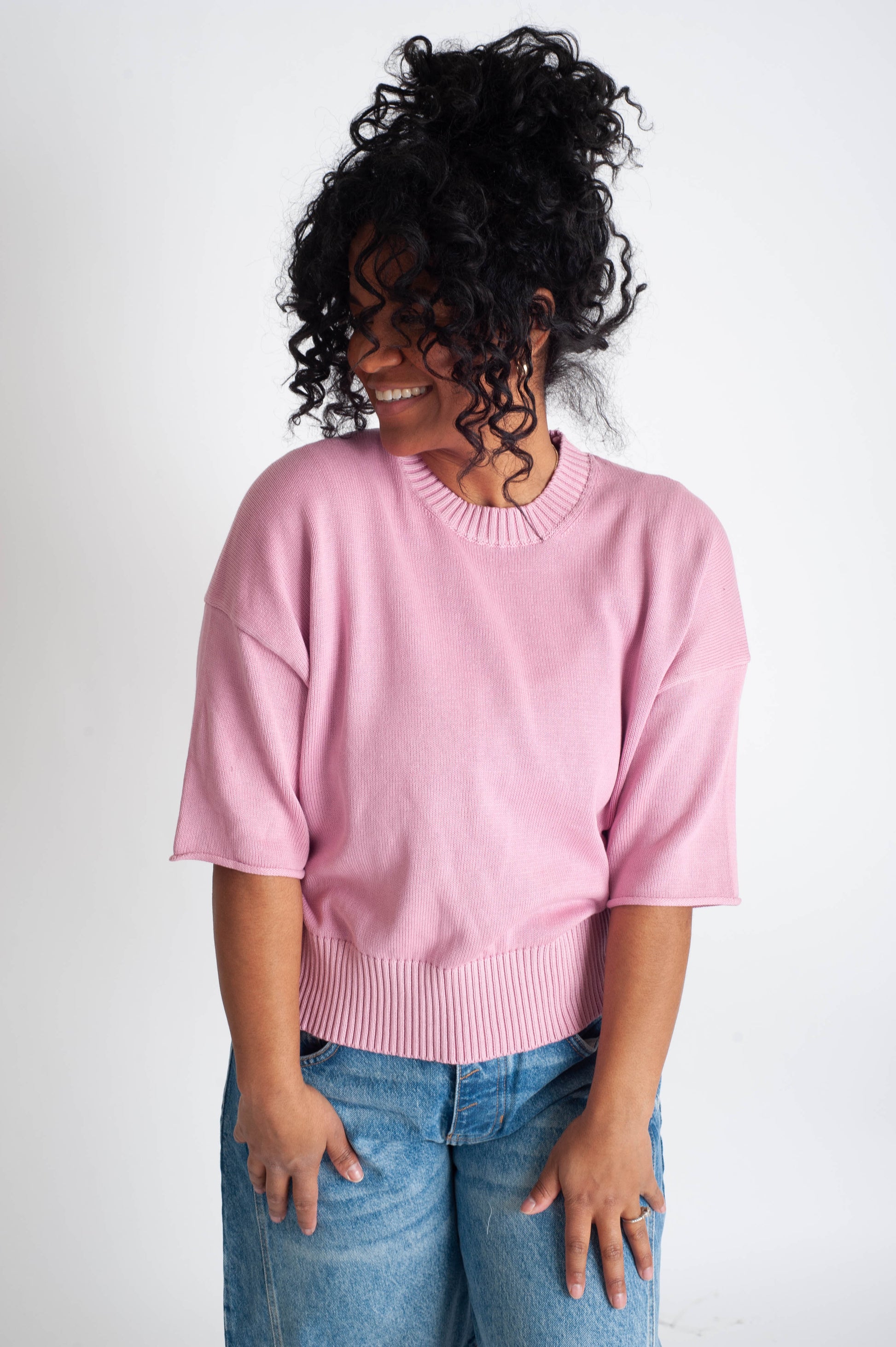 Person wearing a pink sweater and blue jeans on a white background