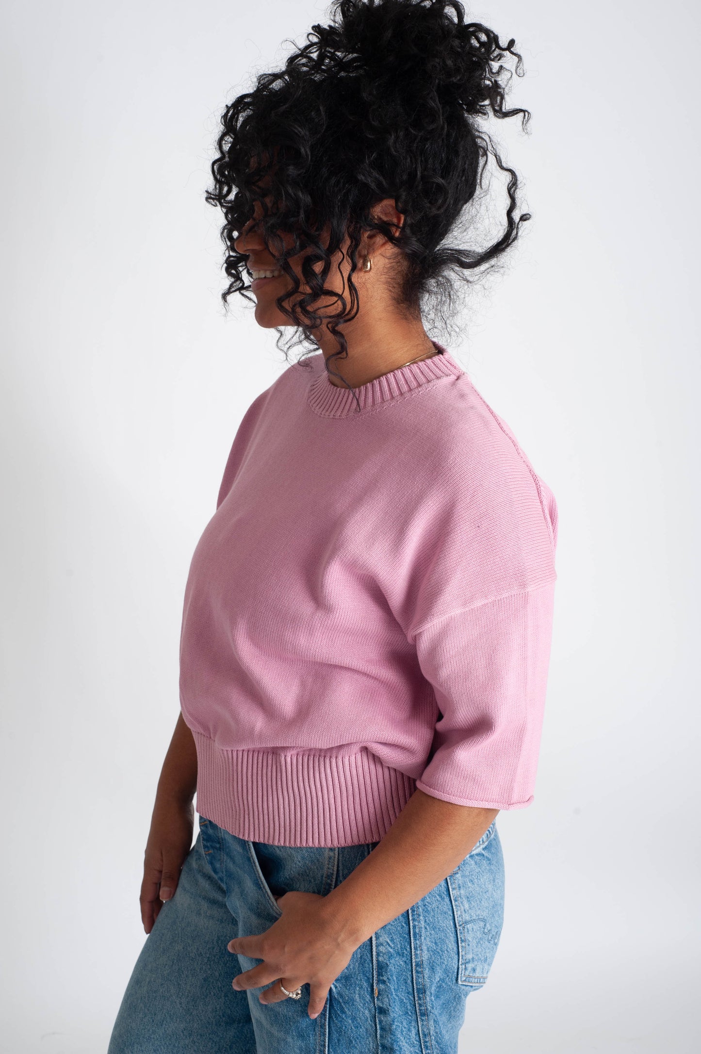 Person wearing a pink sweater and blue jeans on a white background