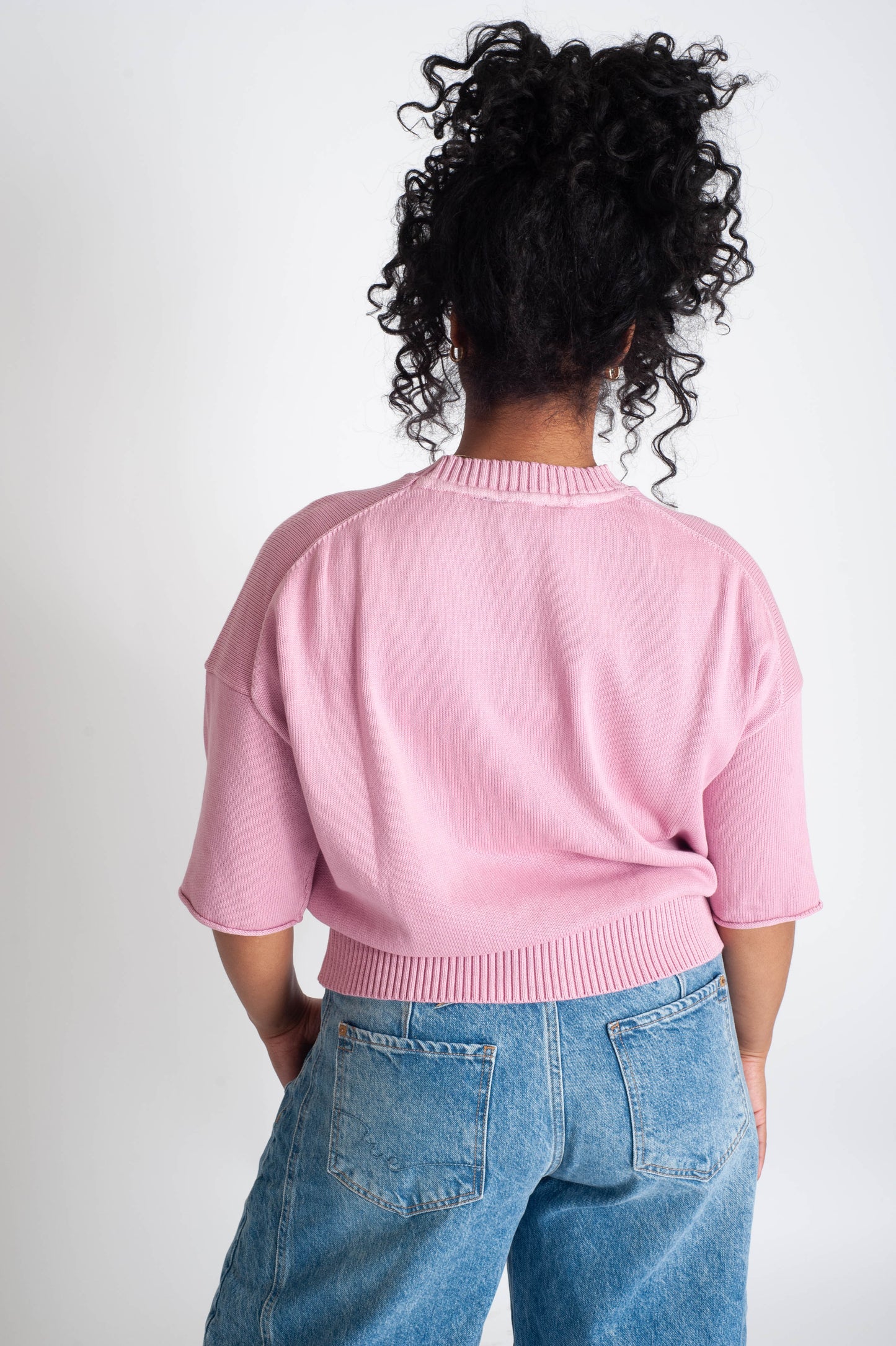 Person wearing a pink sweater and blue jeans against a white background