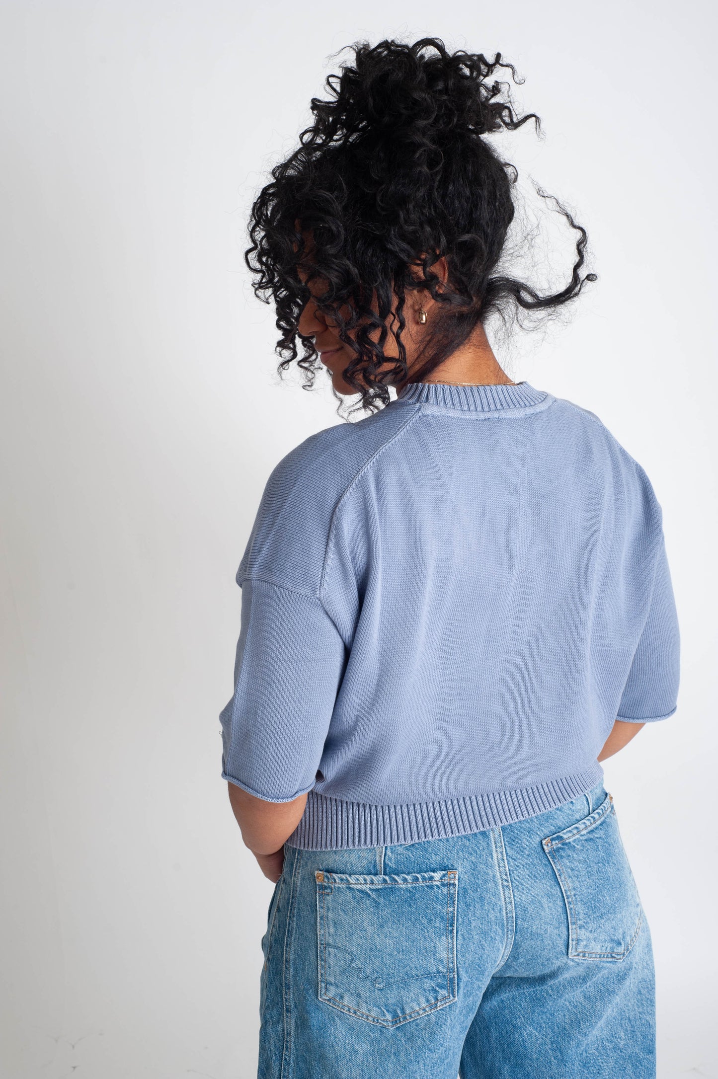 Person wearing a light blue sweater and jeans on a plain background