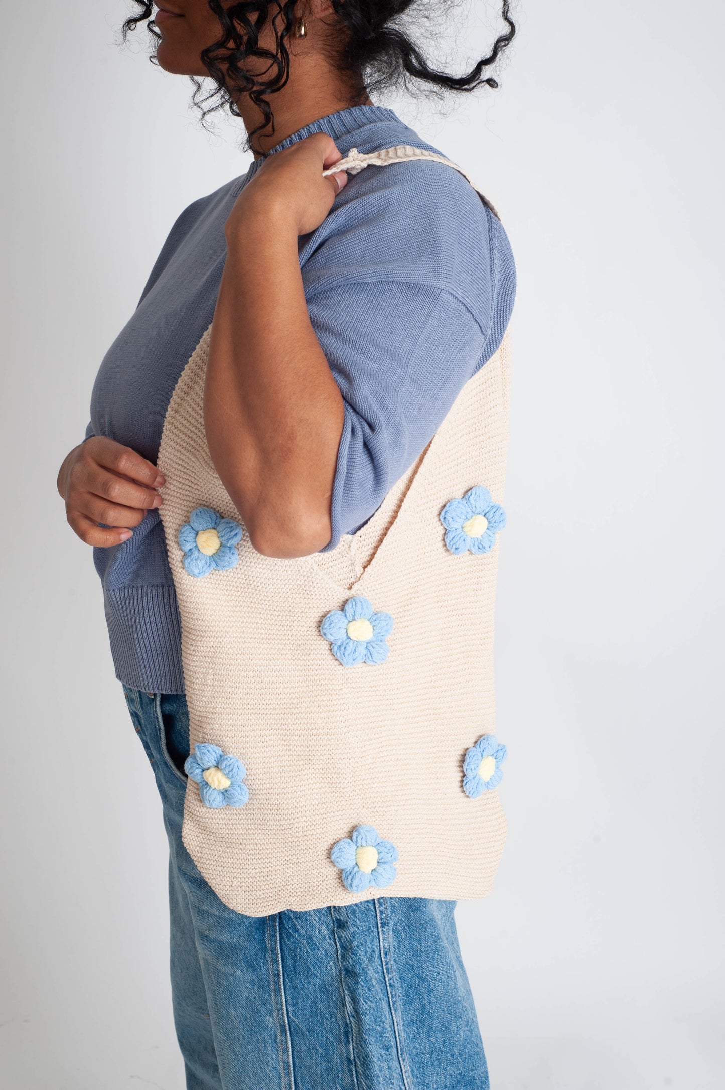 Person wearing a beige tote bag with blue floral patterns on a plain background