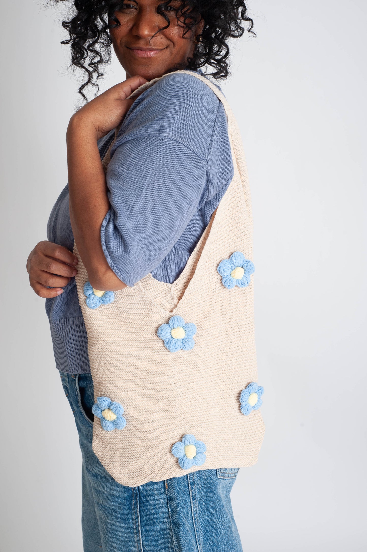Person holding a beige tote bag with blue floral patterns on a plain background
