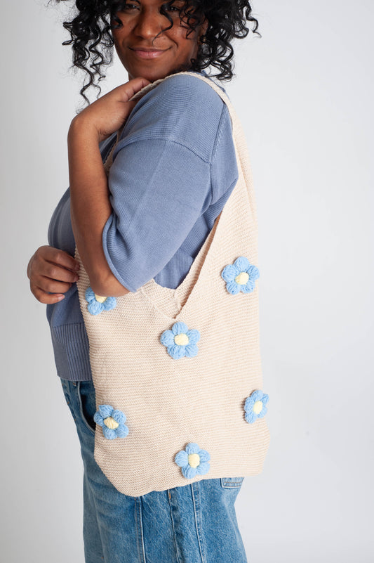 Person holding a beige tote bag with blue floral patterns on a plain background