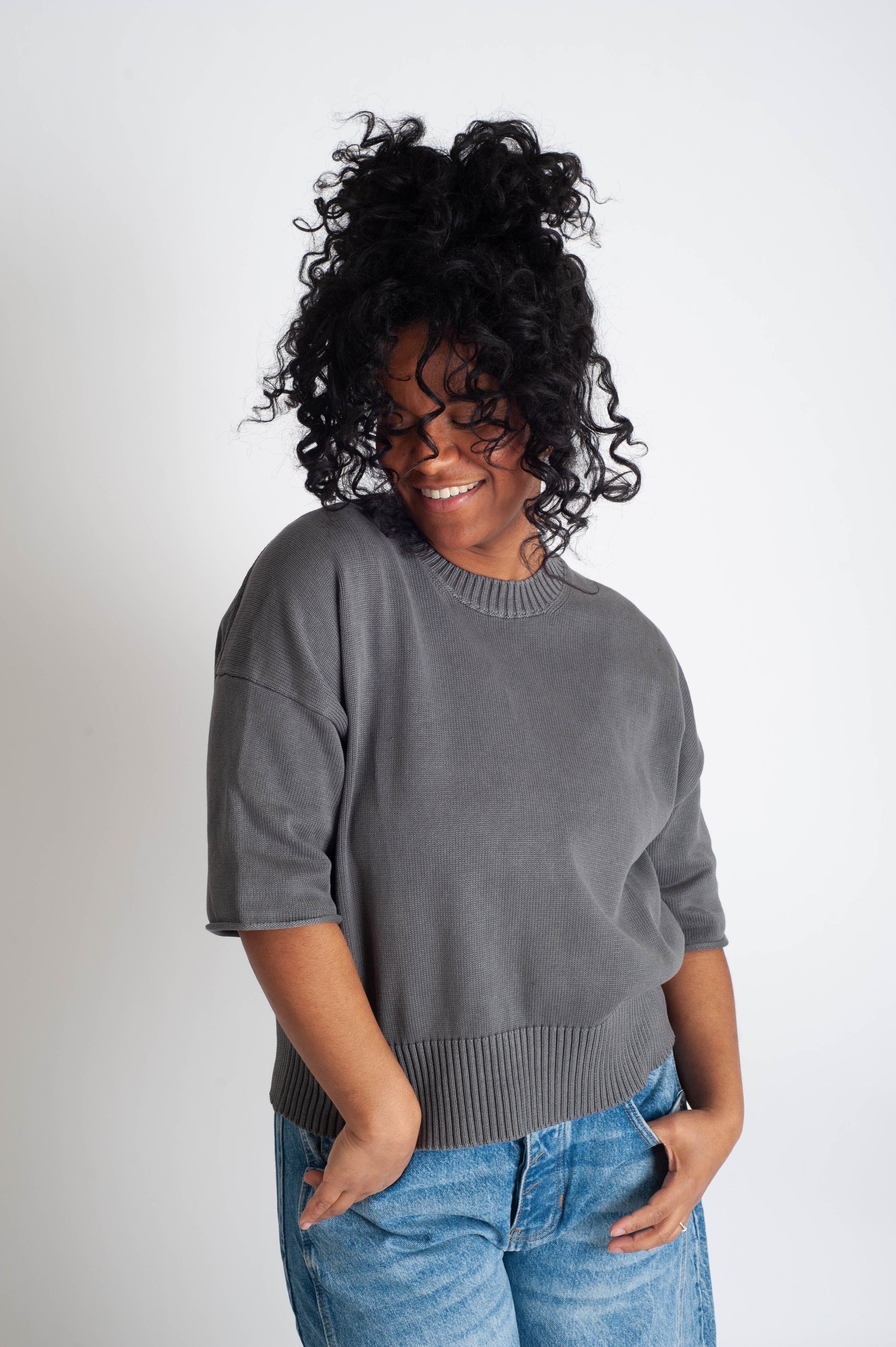 Woman wearing a gray sweater and blue jeans against a white background