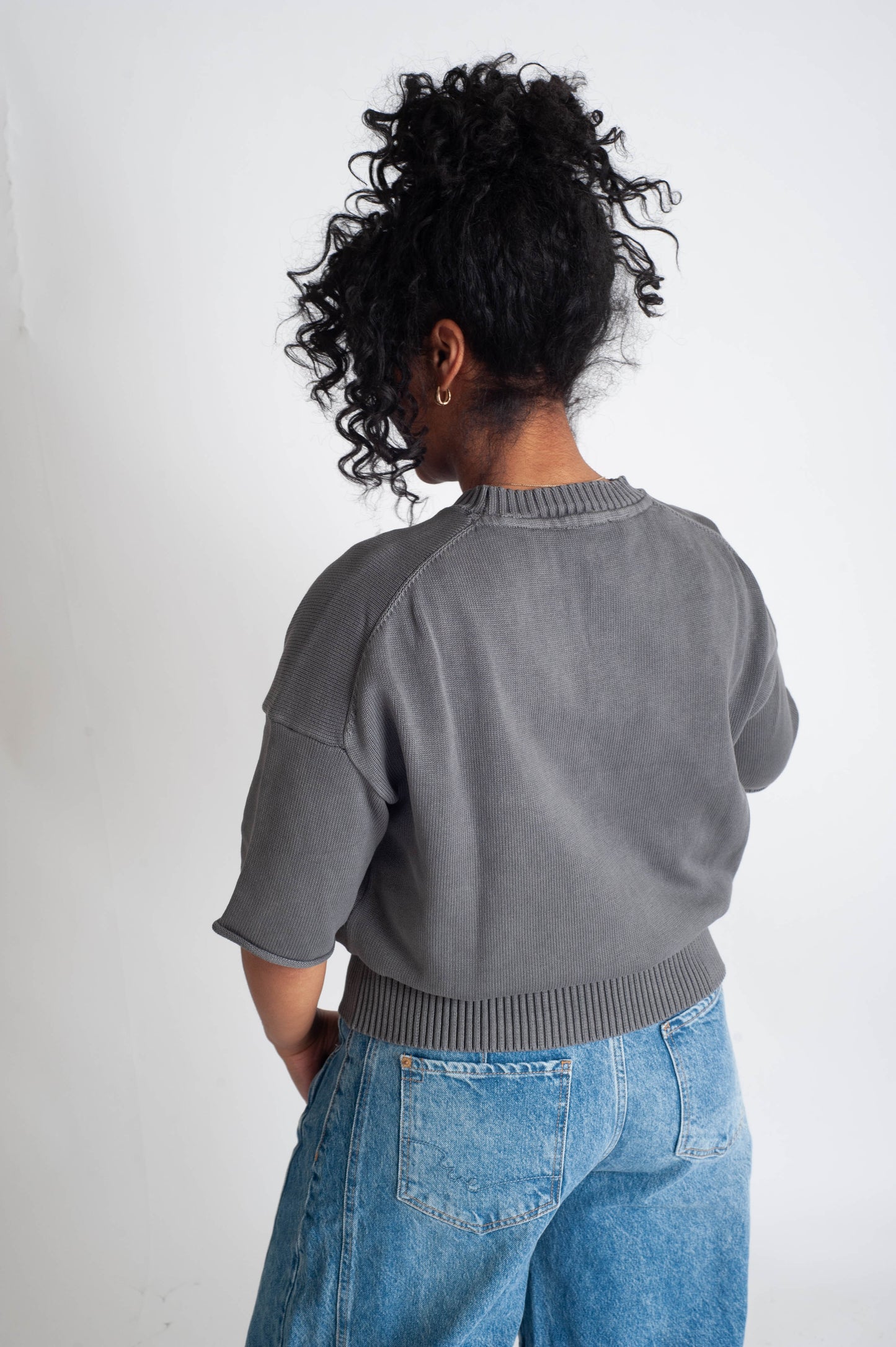 Person wearing a gray sweater and blue jeans from behind on a white background
