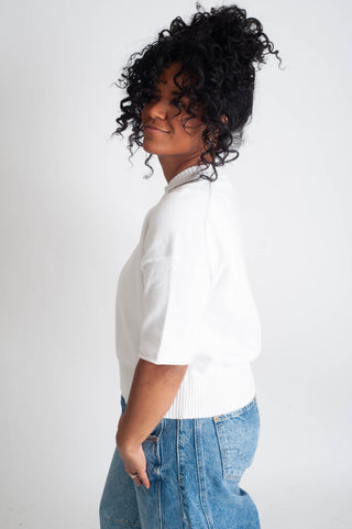 Person wearing a white blouse and blue jeans against a plain background