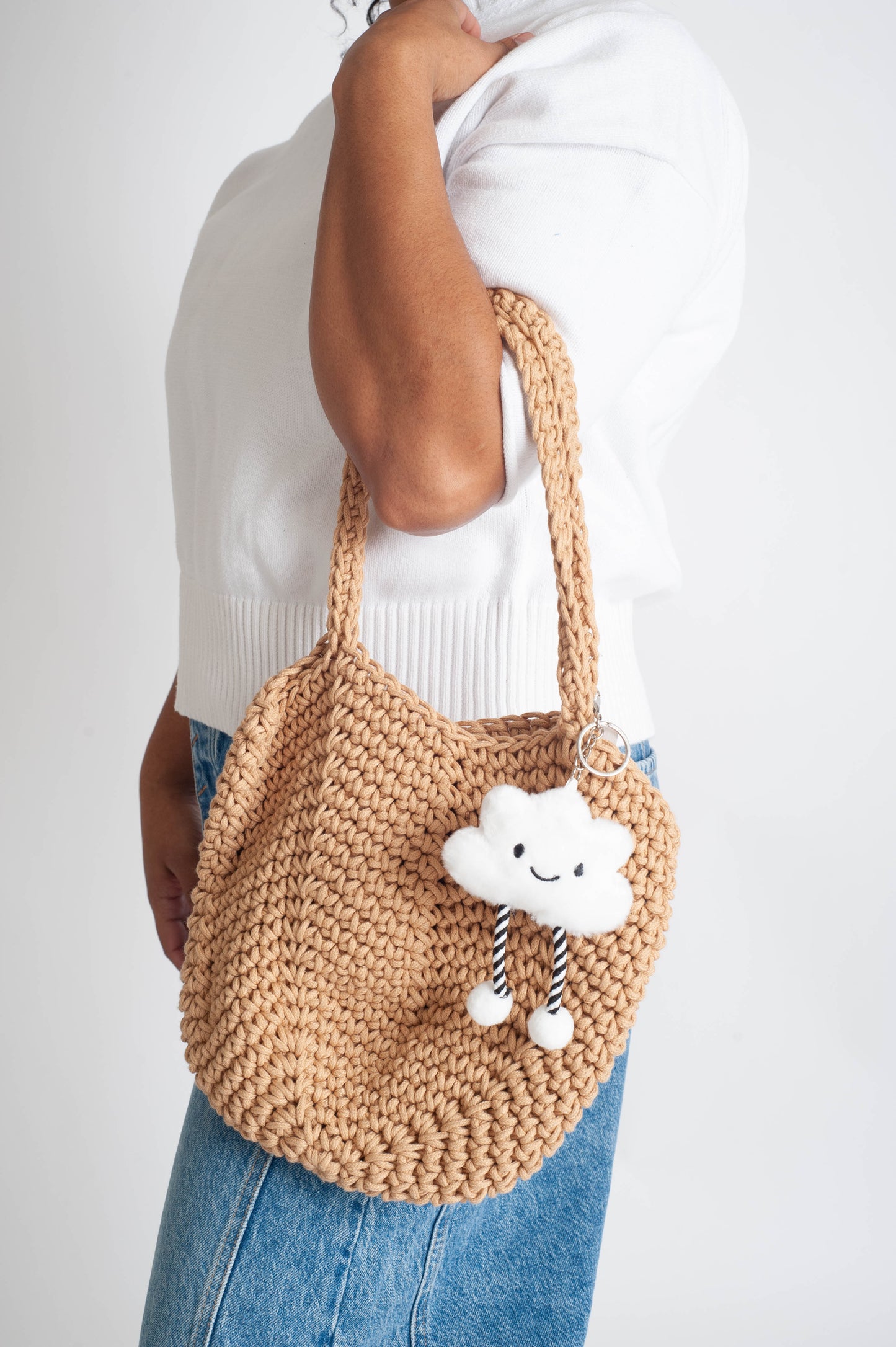 Person holding a woven handbag with a cloud charm on a white background