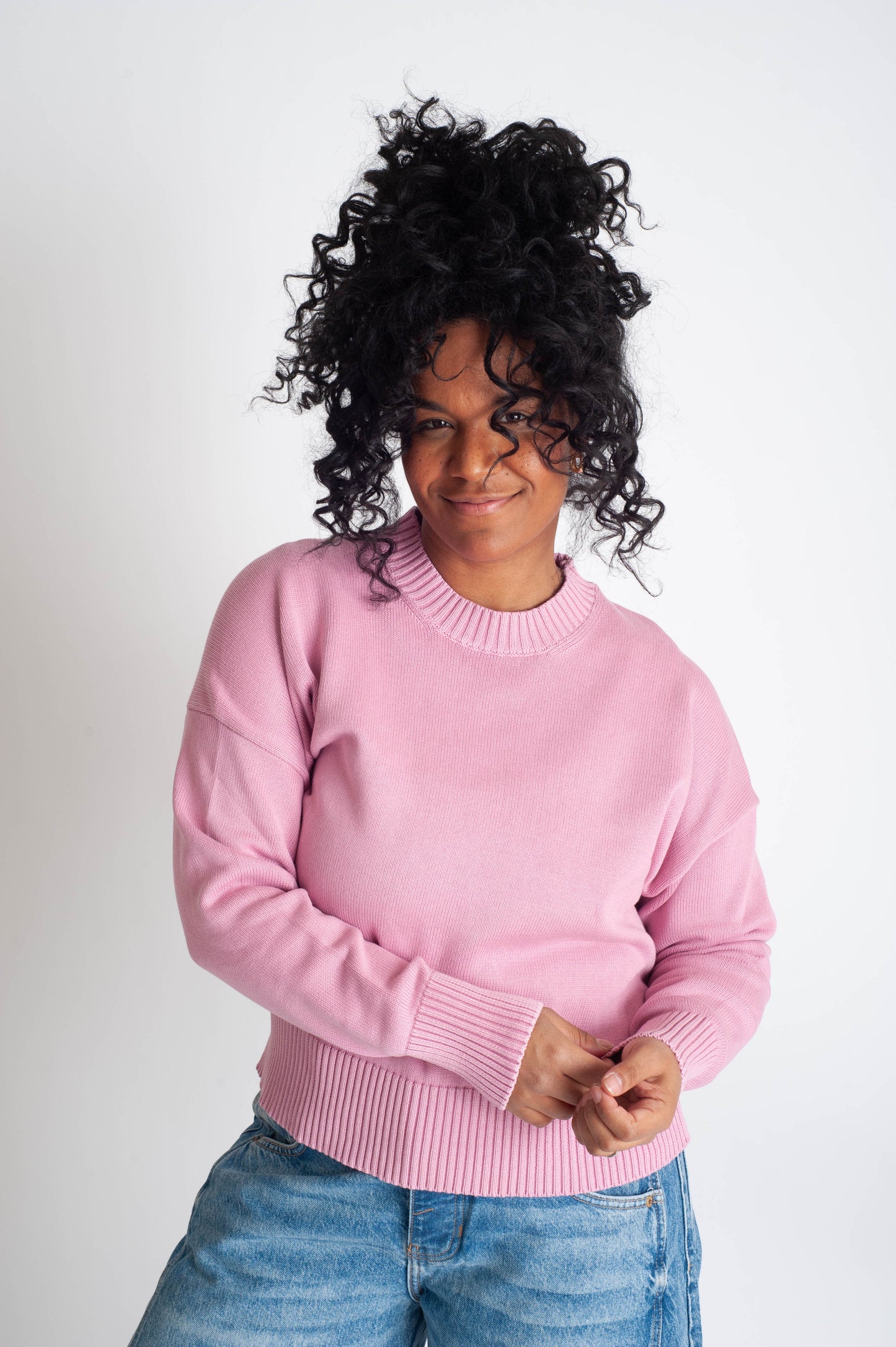Person wearing a pink sweater and blue jeans on a white background