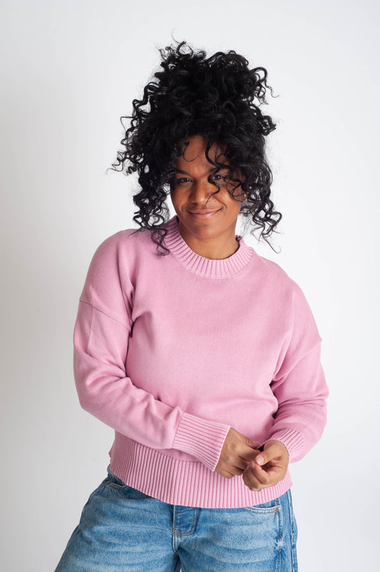 Person wearing a pink sweater and blue jeans on a white background