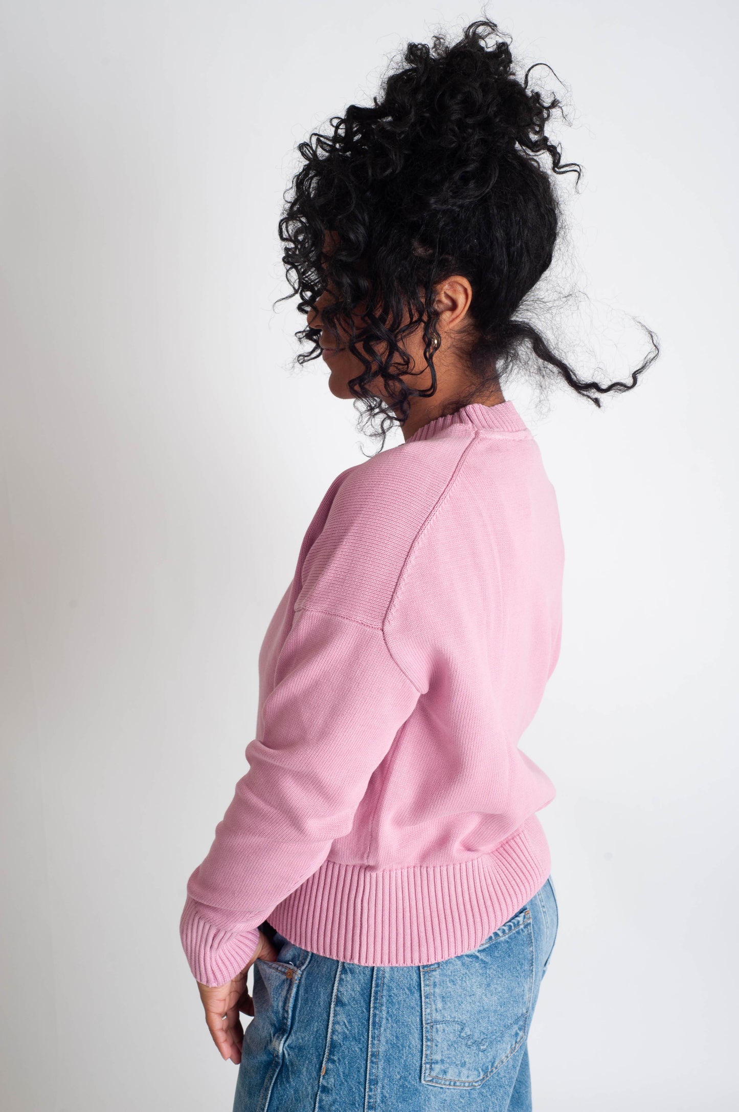 Person wearing a pink sweater and blue jeans against a white background