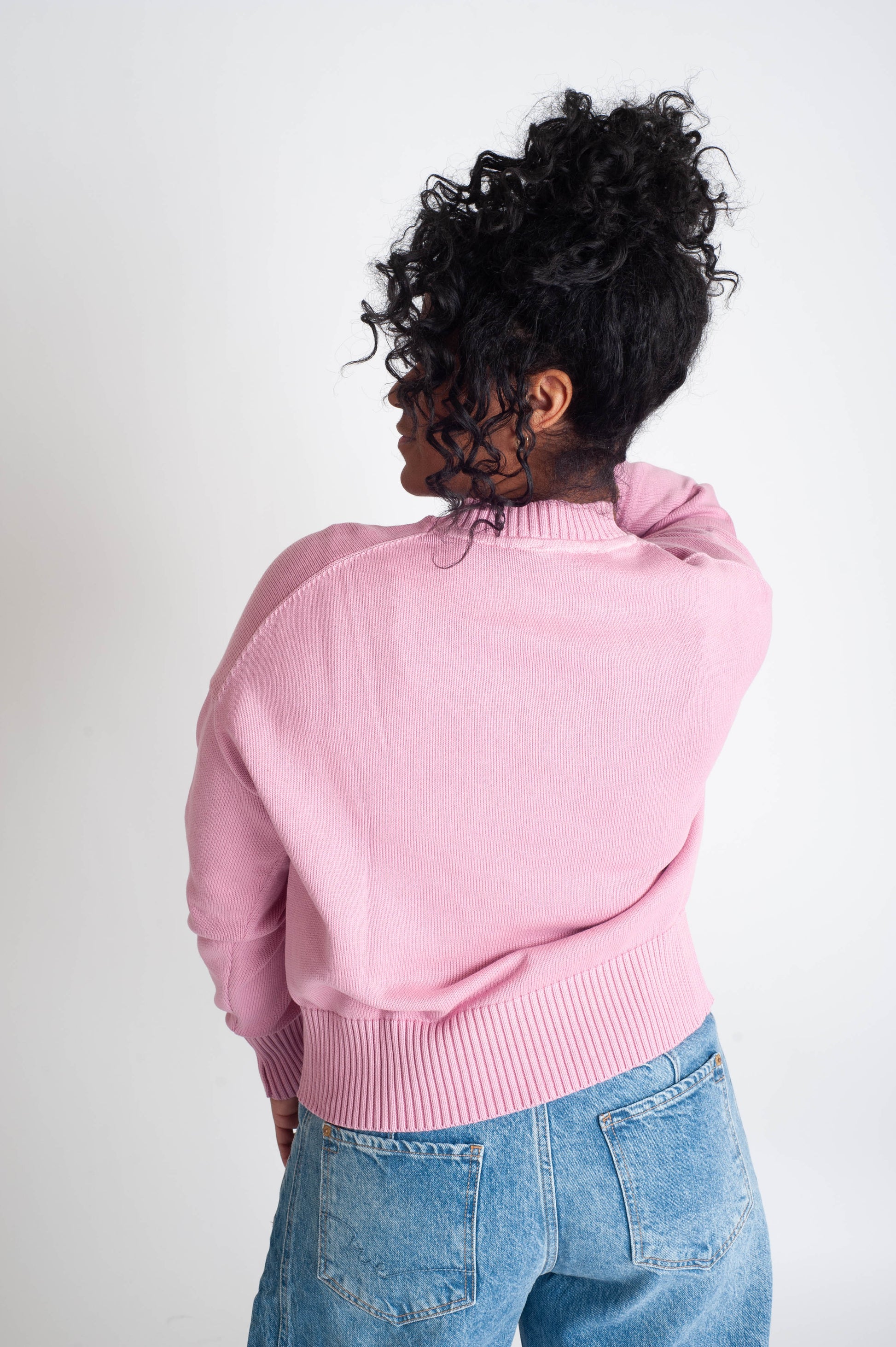 Person wearing a pink sweater and blue jeans from behind on a white background