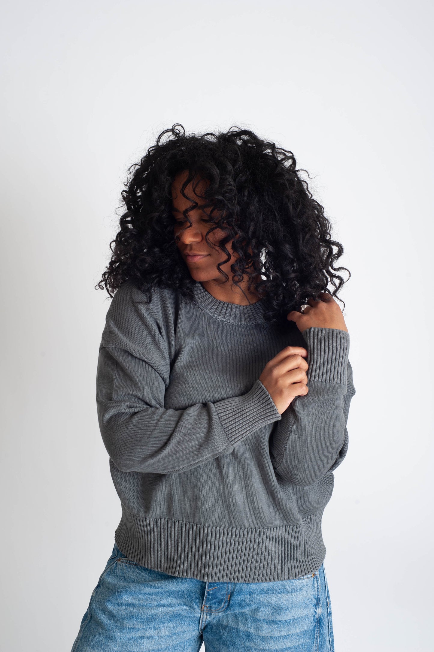 Woman wearing a gray sweater and blue jeans against a white background