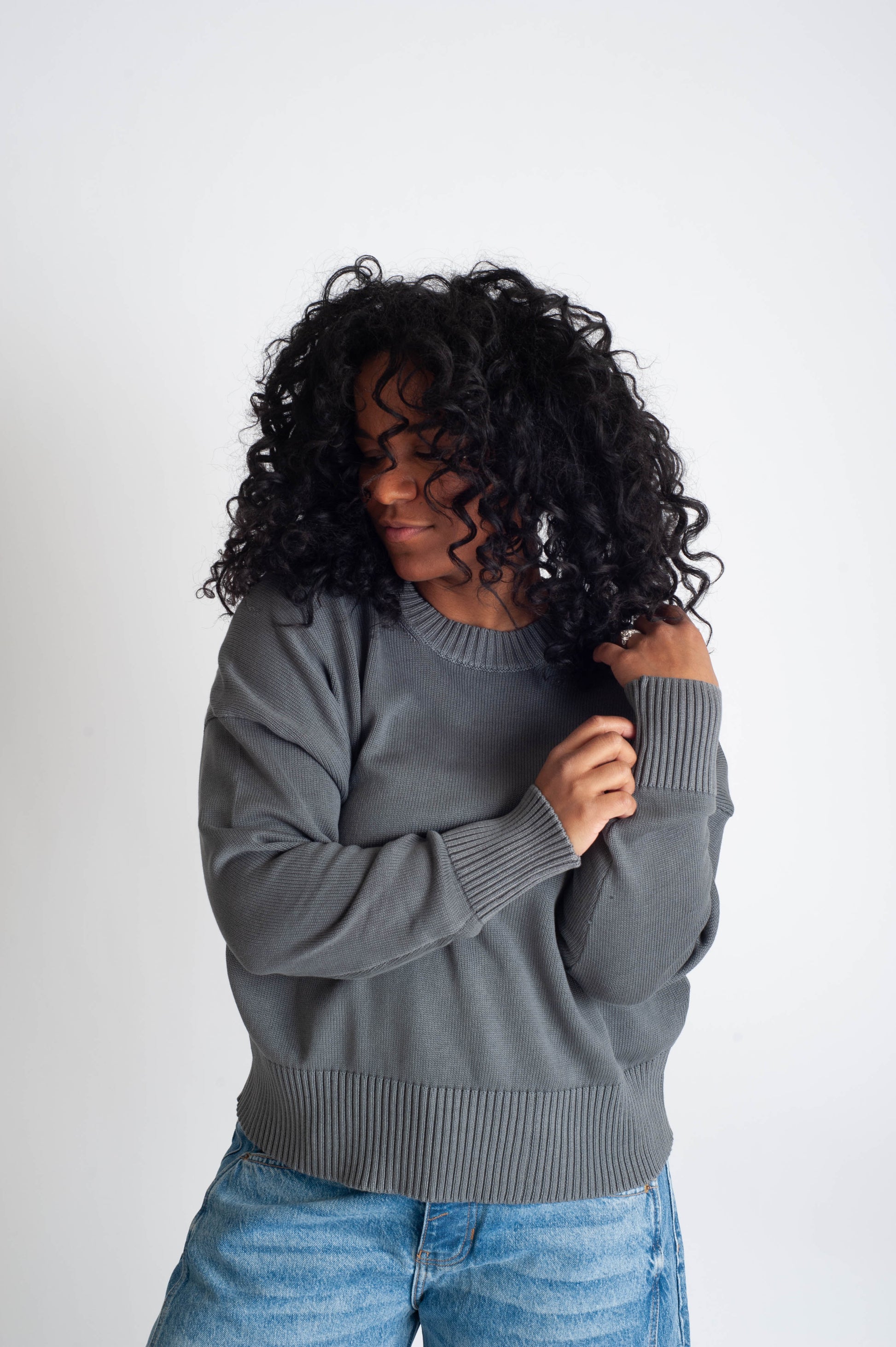 Woman wearing a gray sweater and blue jeans against a white background
