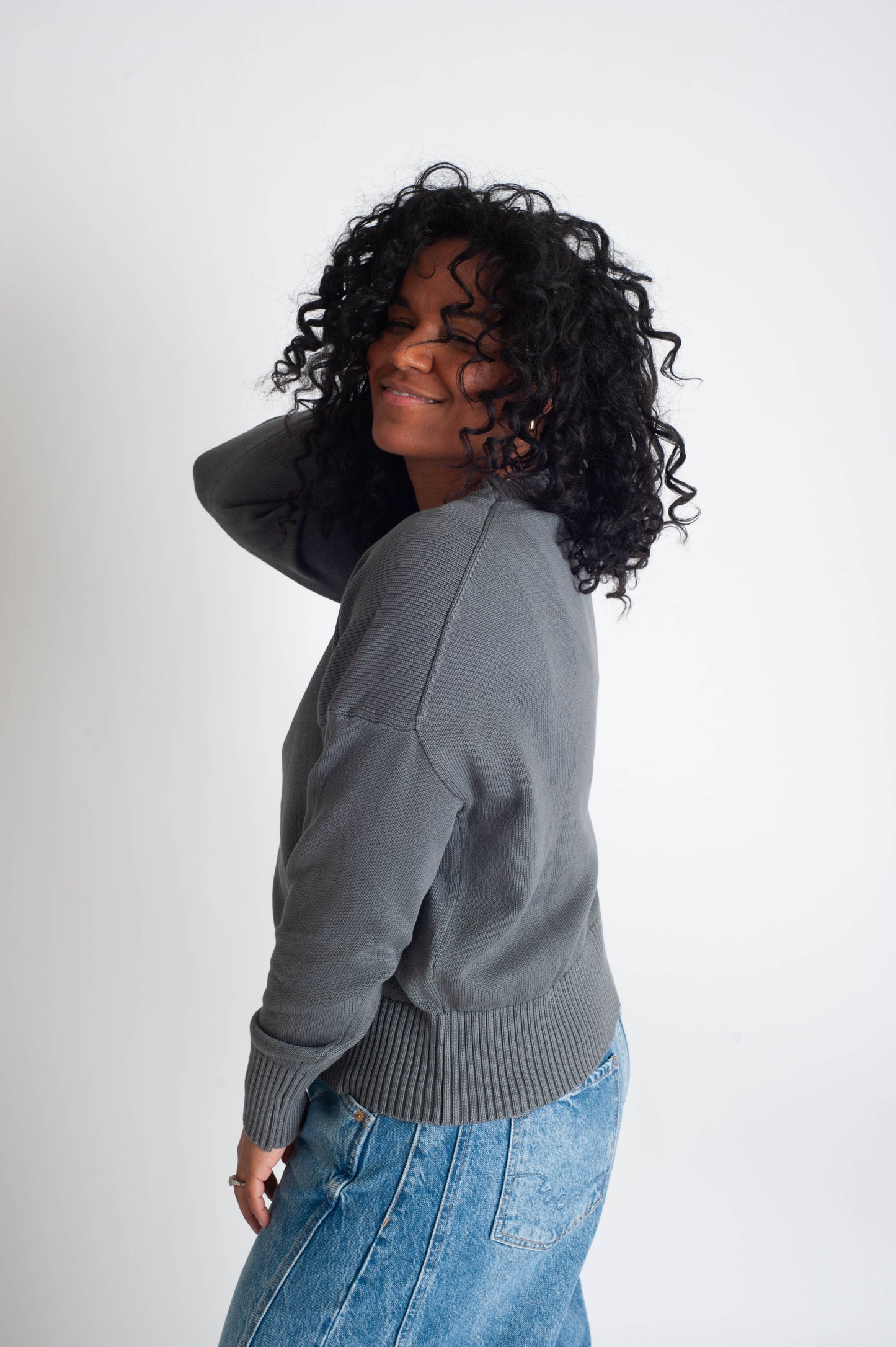 Woman wearing a gray sweater and blue jeans against a white background
