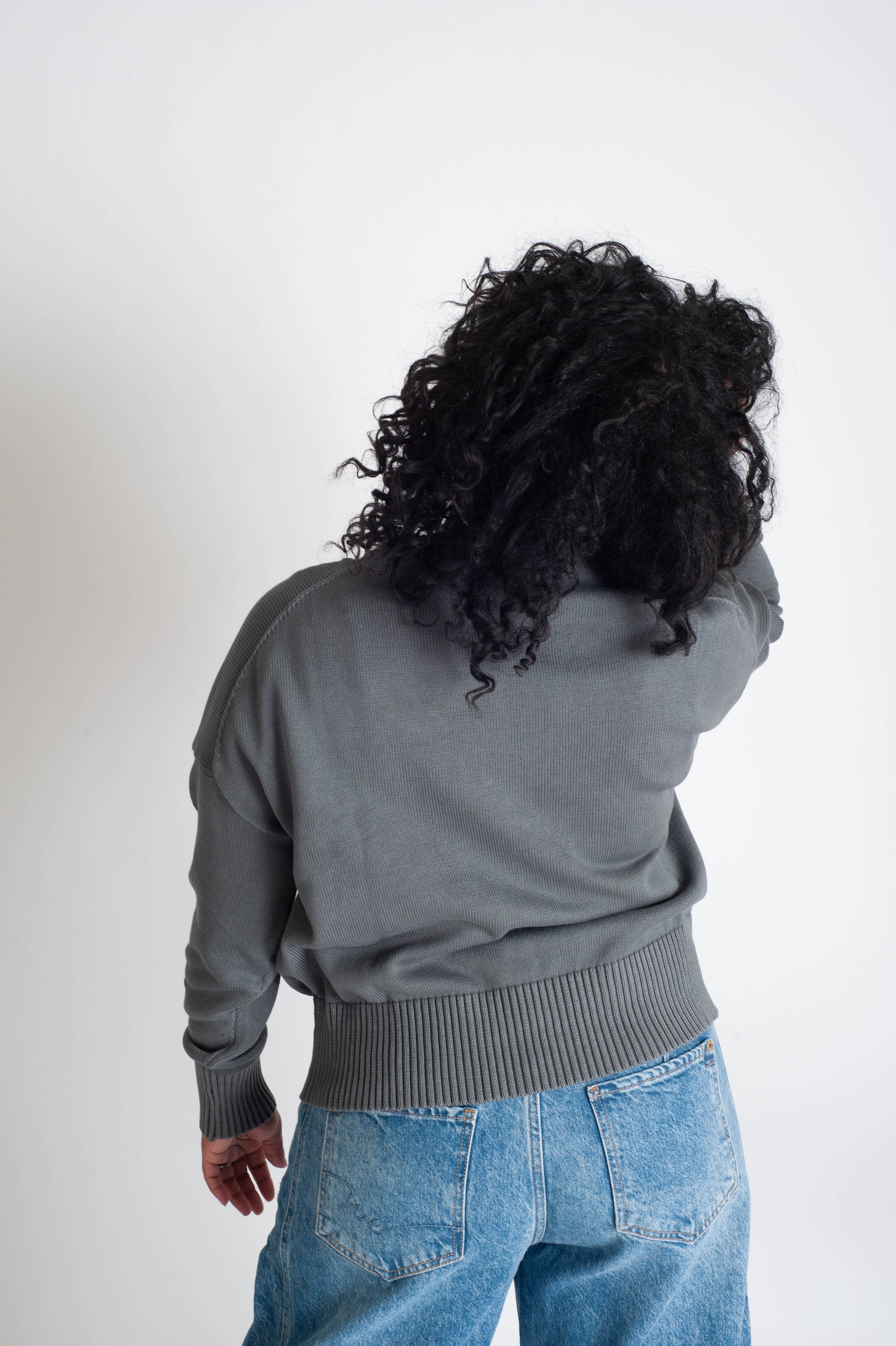 Person wearing a gray sweater and blue jeans from behind on a white background