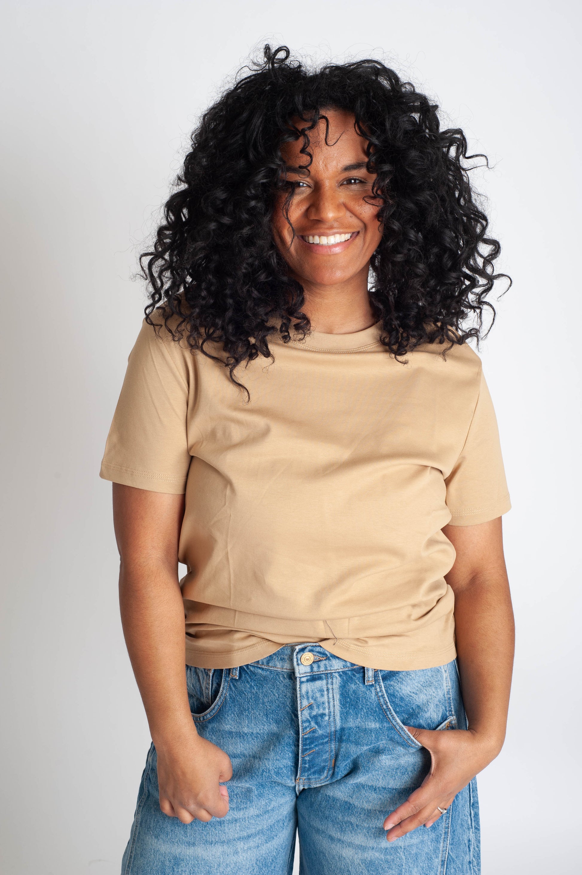 Woman wearing a beige t-shirt and blue jeans against a white background
