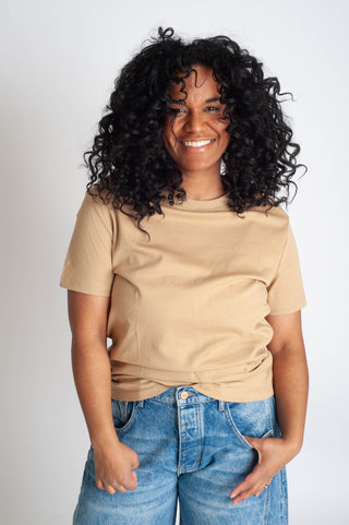 Woman wearing a beige t-shirt and blue jeans against a white background
