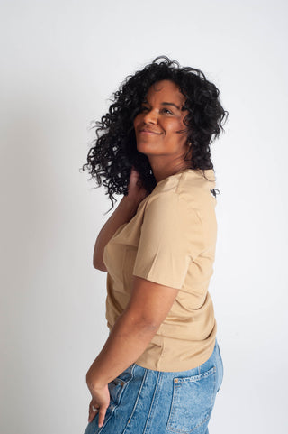 Woman wearing a beige top and blue jeans against a white background
