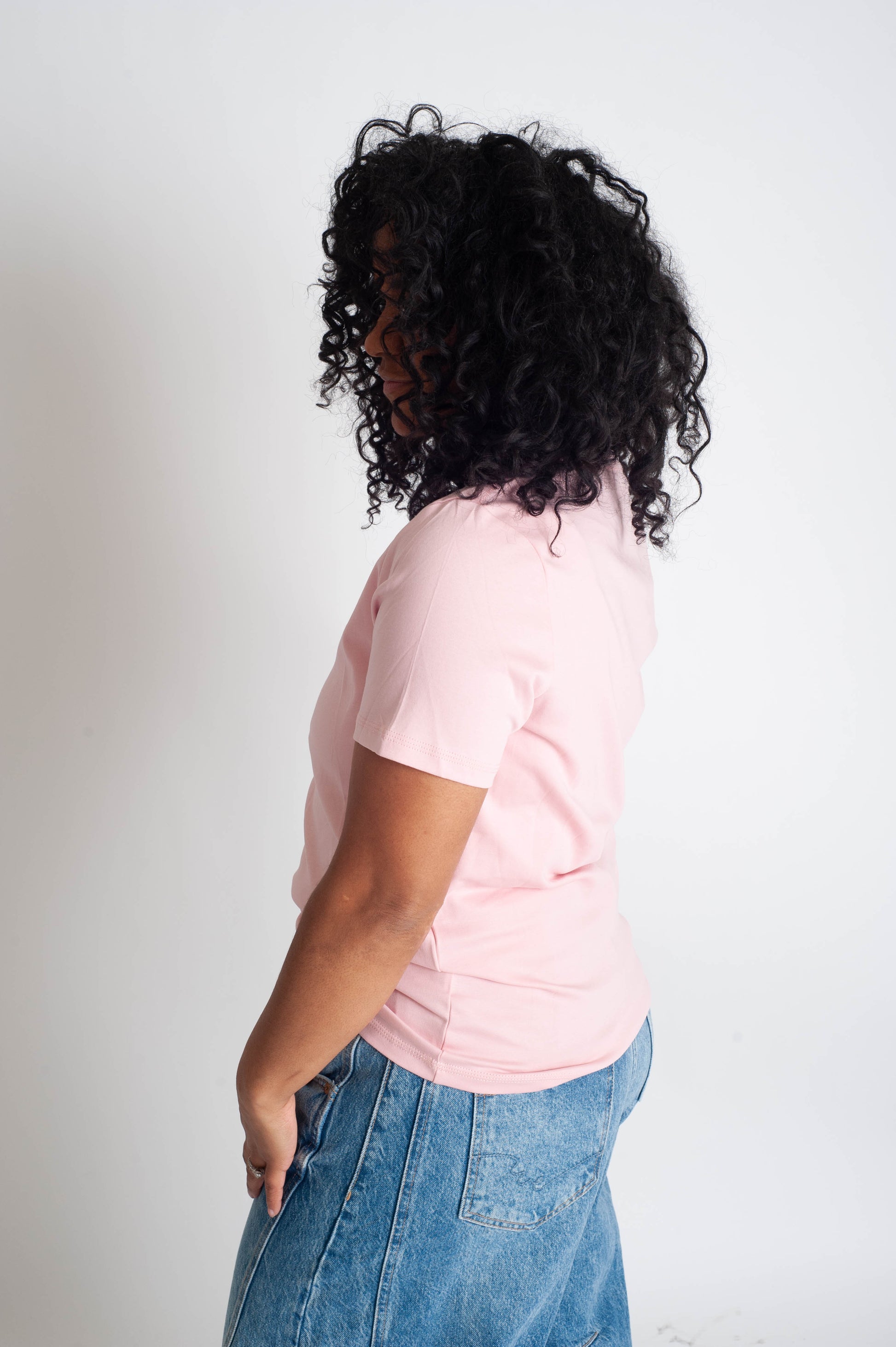 Person wearing a pink t-shirt and blue jeans against a white background