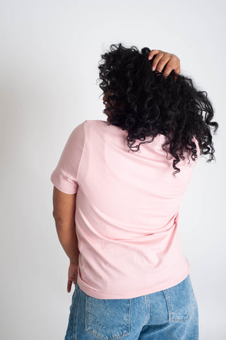 Person wearing a pink shirt and blue jeans with their back to the camera on a plain background