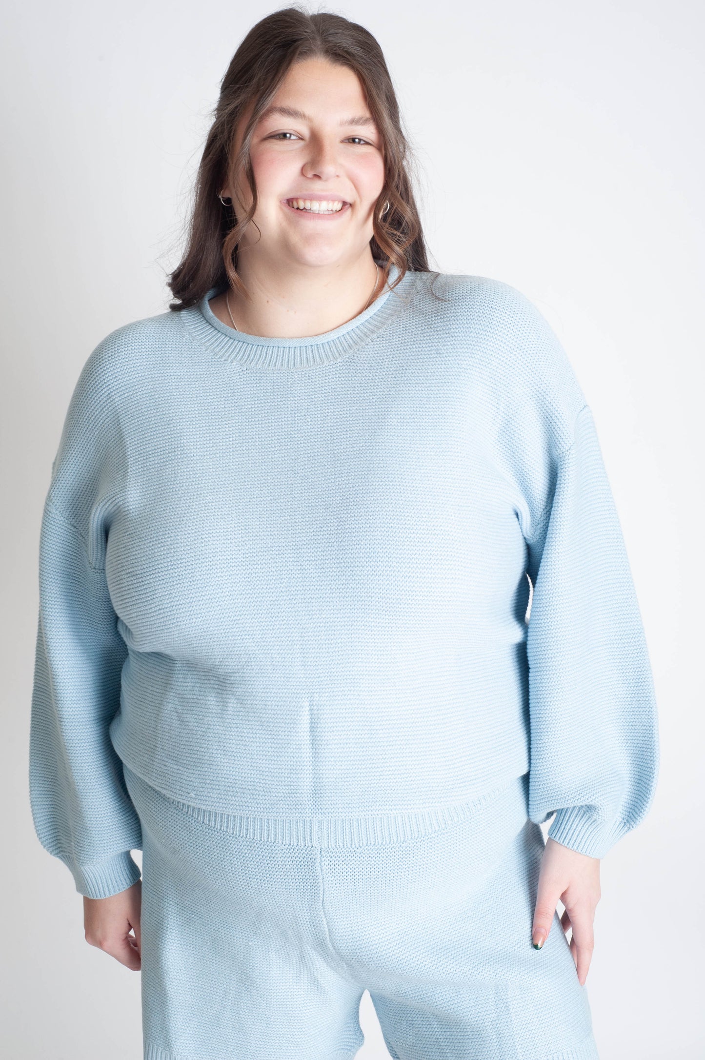 Person wearing a light blue sweater and pants set on a plain background