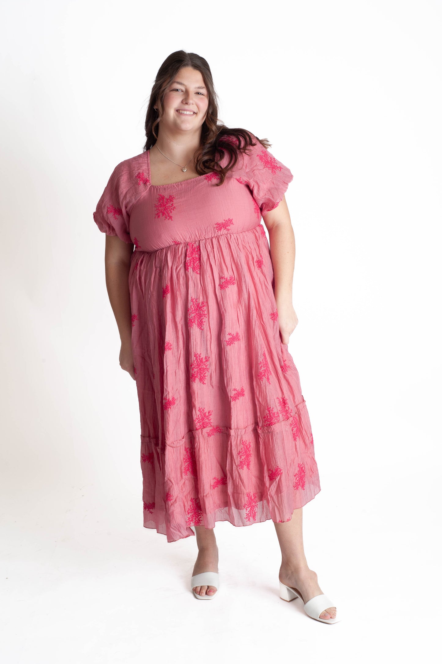Woman wearing a pink dress with floral patterns on a white background