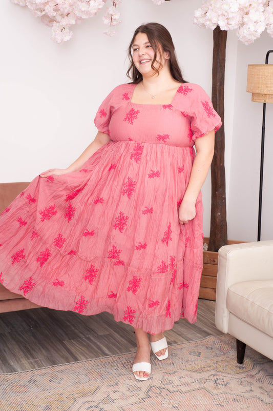 Woman wearing a pink dress with floral patterns in a room with decorative elements.