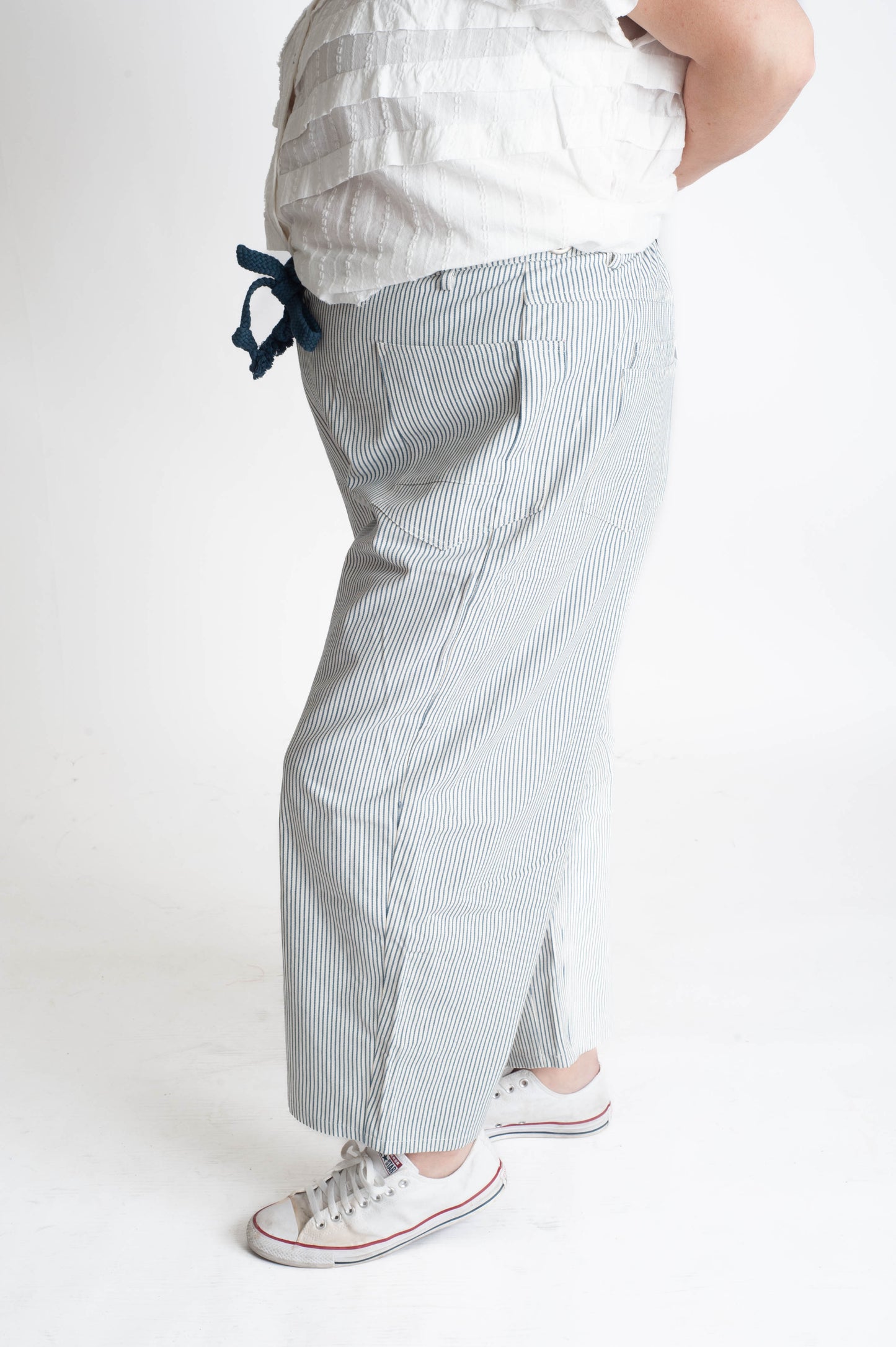 Person wearing light blue striped pants and a white top on a white background