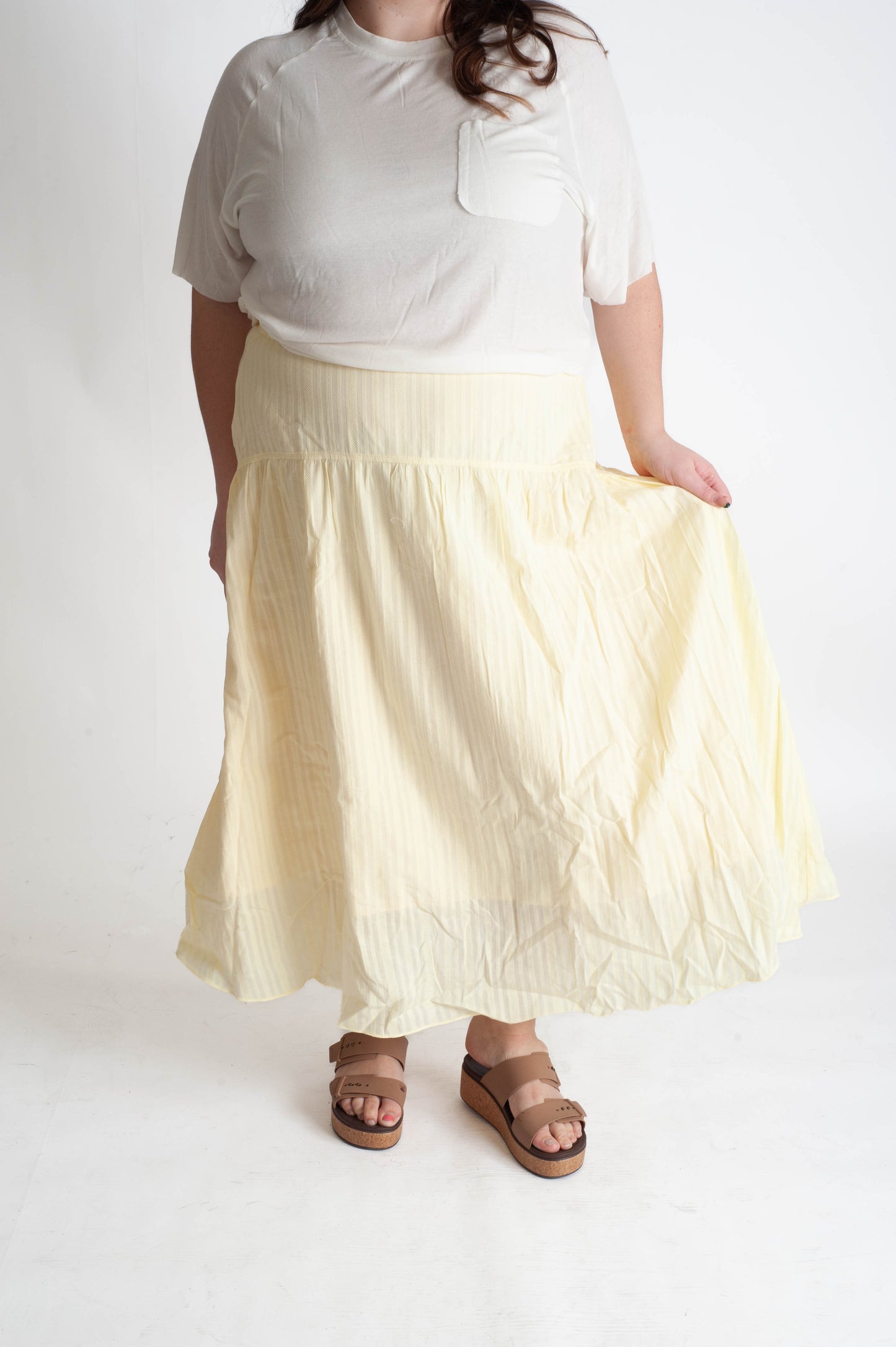 Person wearing a white t-shirt and light yellow skirt on a white background