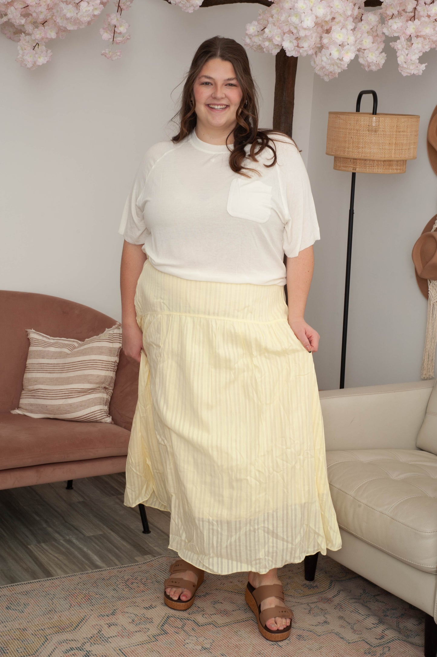 Woman in a white blouse and yellow skirt standing in a living room with a couch and lamp in the background.