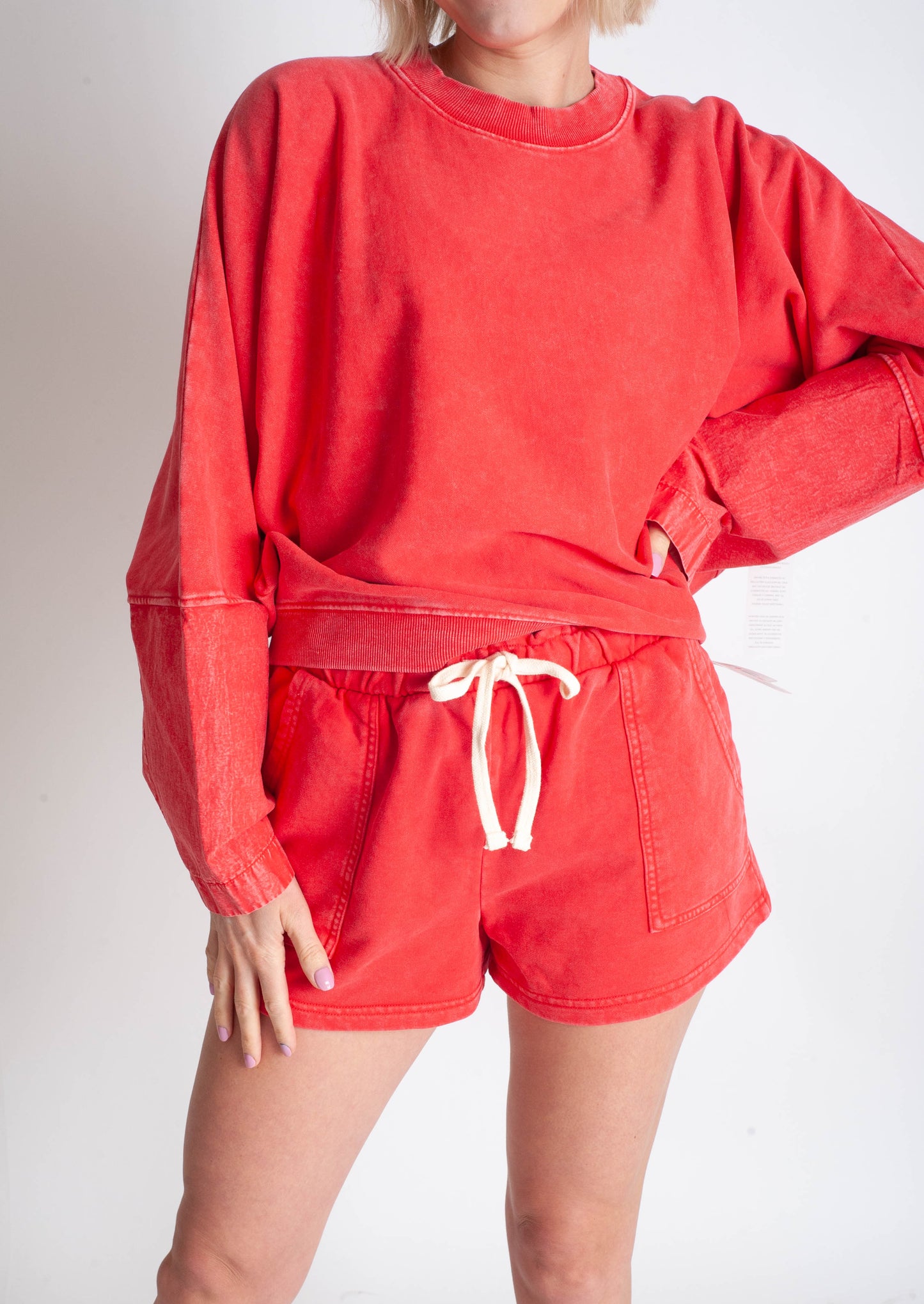 Person wearing a red sweatshirt and shorts set on a plain background