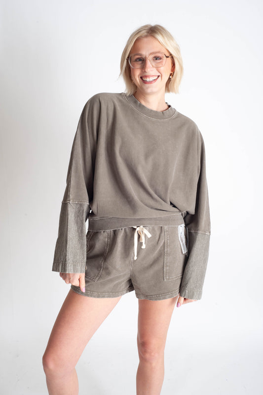 Woman wearing a matching olive green sweatshirt and shorts set on a white background