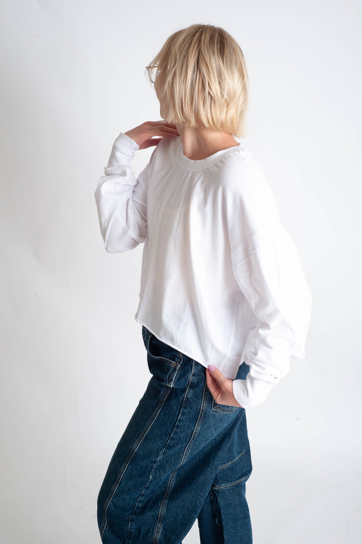 Person wearing a white sweater and blue jeans against a white background
