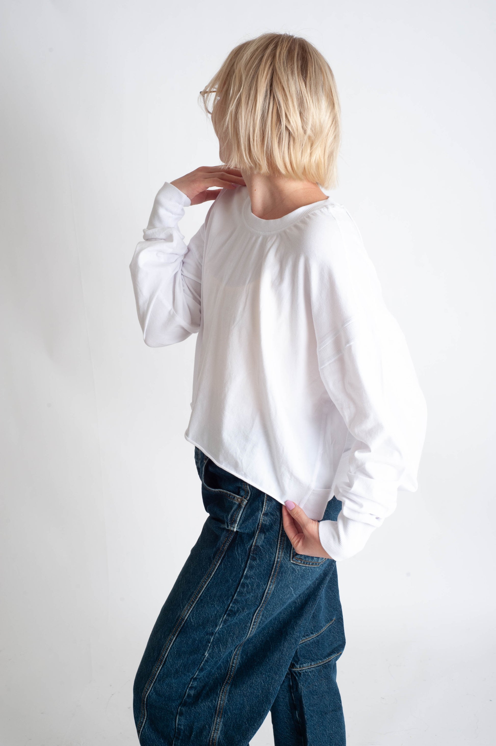 Person wearing a white sweater and blue jeans against a white background