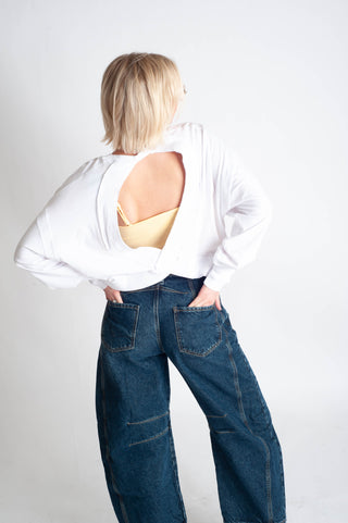 Person wearing a white shirt with cut-out design and blue jeans on a plain background