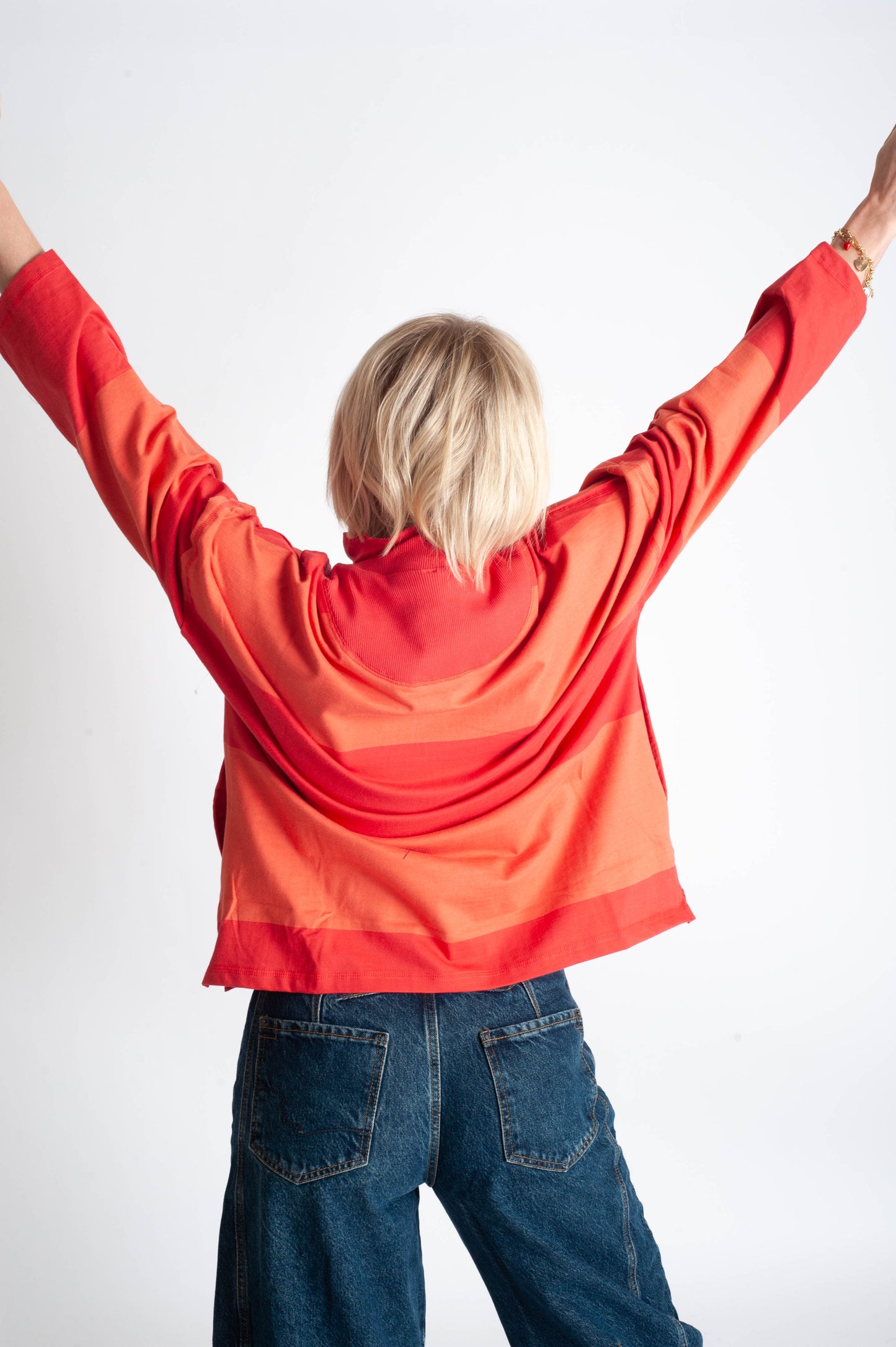 Person wearing a red hoodie and blue jeans with arms raised on a white background
