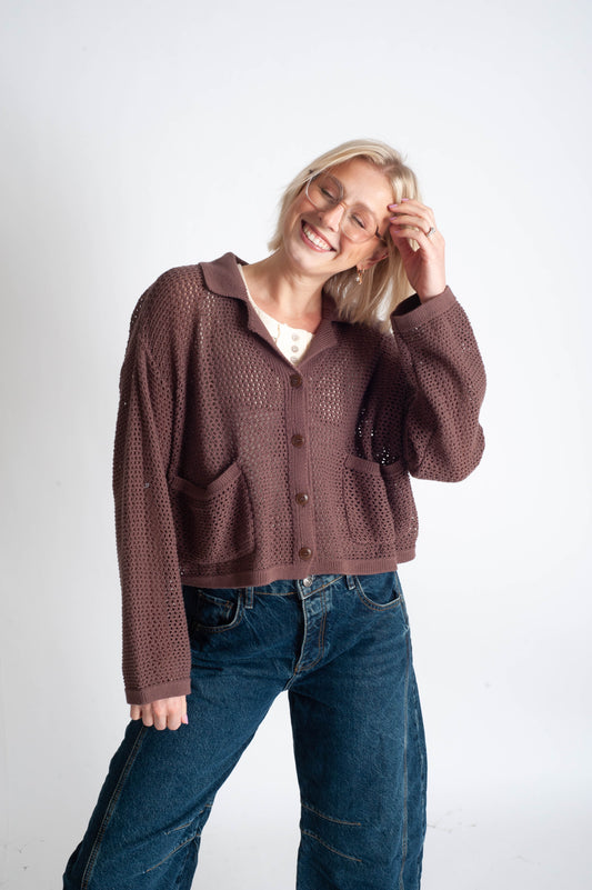Woman wearing a brown knitted cardigan and blue jeans on a white background