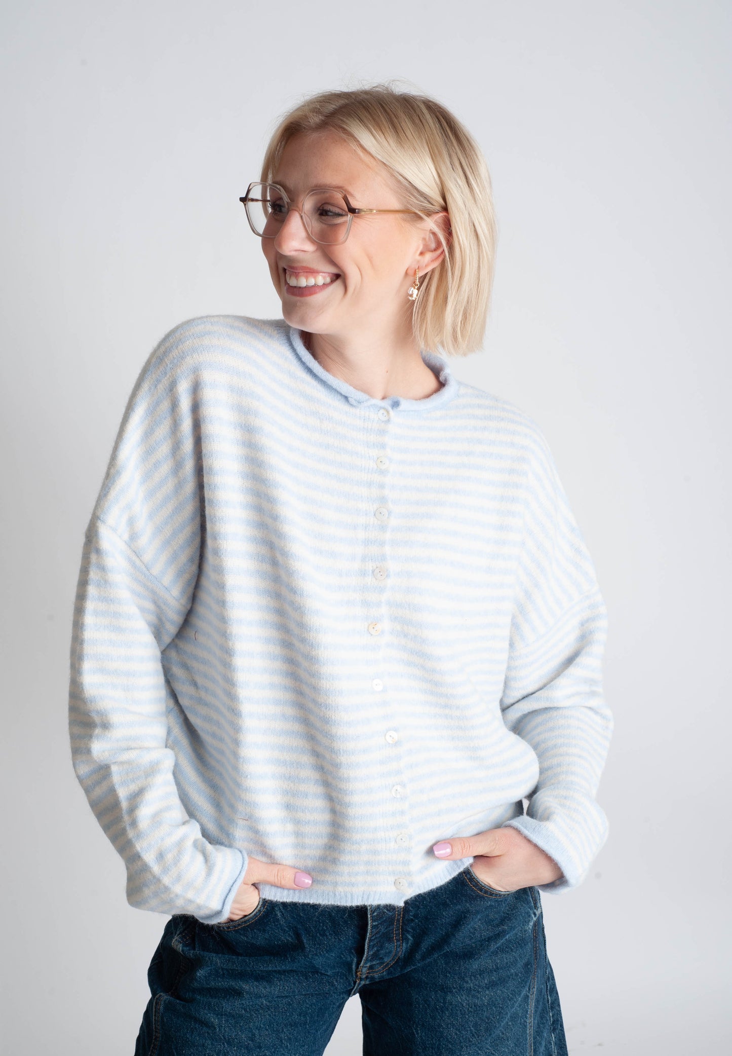 Woman wearing a light gray striped sweater and blue jeans against a white background