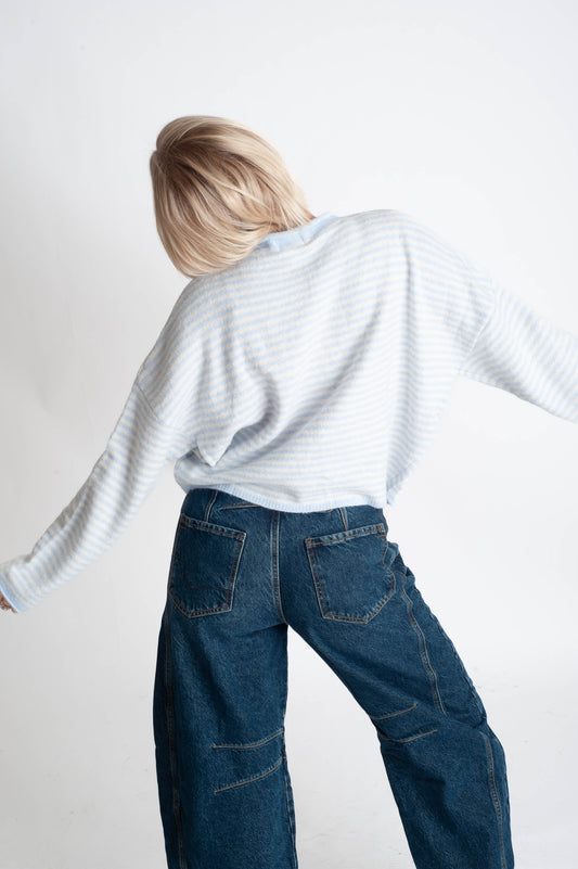 Person wearing a light gray sweater and blue jeans against a white background