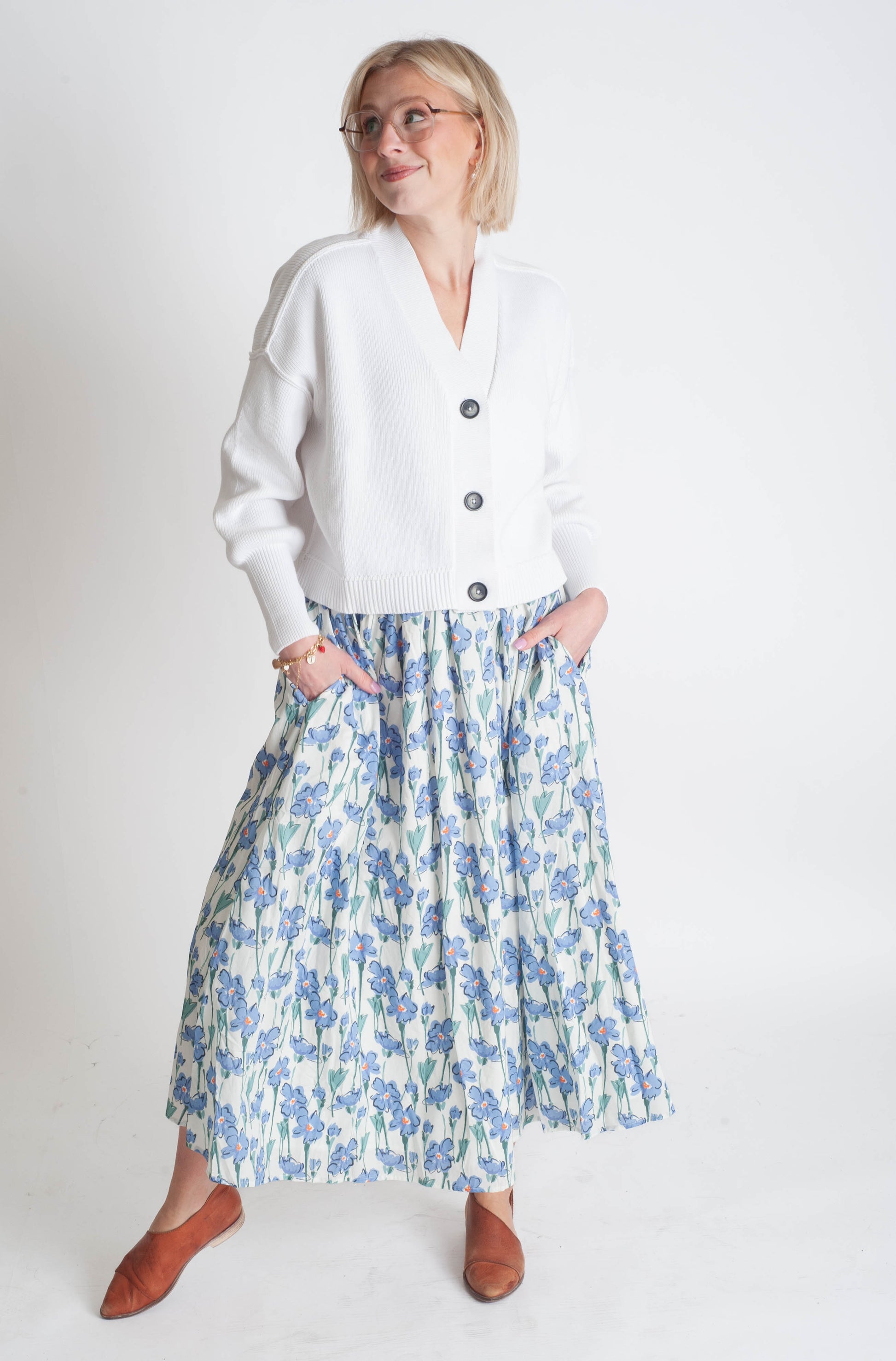 Woman wearing a white cardigan and floral skirt on a white background